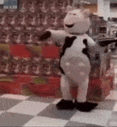 a cow mascot is dancing in a store in front of a shelf of cans .