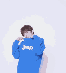 a young man wearing a blue jeep sweatshirt covering his face