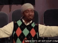 a man wearing a plaid sweater and a beanie is sitting in a theater with his arms outstretched ..