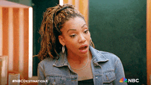 a woman with dreadlocks is wearing a denim jacket and earrings