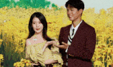 a man and a woman are standing next to each other in front of a field of yellow flowers