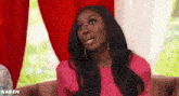 a woman is sitting on a couch wearing a pink dress and earrings .