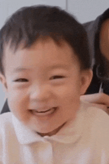a baby is smiling and looking at the camera while sitting next to a woman .