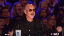 a bald man stands in front of a crowd with a cup that says izza on it