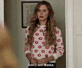 a young girl is standing in a doorway wearing a sweater with flowers on it and talking to someone .