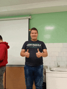 a young man wearing a jean pascale t-shirt gives a thumbs up