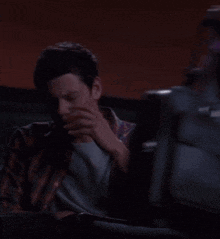 a man covering his face with his hand while sitting in a dark room
