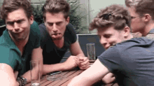 a group of young men are sitting at a table making funny faces and drinking beer .