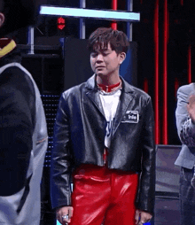 a man wearing a black leather jacket and red pants has a name tag that says into