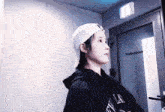 a woman wearing a white hat and a black hoodie is standing in front of a door that says studio m-lab