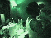 a man in a white tank top is standing in a dark room with a green light behind him
