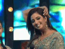 a woman in a blue and gold dress is smiling and touching her hair