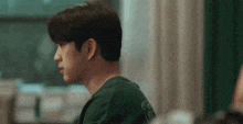 a young man in a green shirt is sitting in front of a window and looking at something .