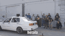 a group of people are standing around a white car with hetala written on it