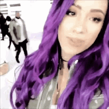 a woman with purple hair is taking a selfie in front of a group of people .