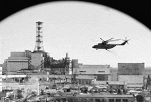 a black and white photo of a helicopter flying over a building