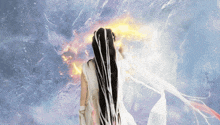 a woman with long black hair and a white dress stands in front of a fire