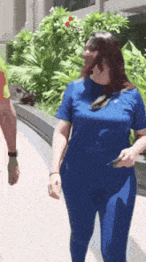 a woman in a blue shirt and pants is walking down a sidewalk
