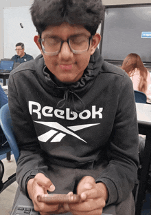 a boy wearing a black reebok sweatshirt looks at his cell phone