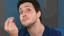 a man in a blue shirt is making a funny face with his hand