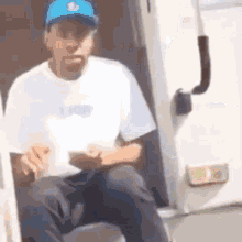 a man wearing a blue hat and a white shirt is sitting on a stool .