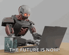 a robot is sitting in front of a laptop with the words the future is now below it