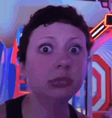 a woman with short hair is making a funny face while standing in front of a neon sign .