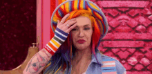 a woman with long red hair is wearing a colorful hat and a rainbow wristband .