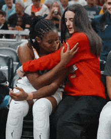 a woman in a red sweatshirt is hugging a basketball player in a crowd .