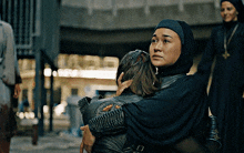 a woman in a black hijab is hugging a child