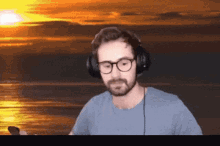 a man wearing glasses and headphones is standing in front of a sunset over the ocean