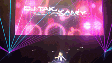 dj tak kamiy performs on stage with a large screen behind him