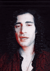 a man with long curly hair and red eyes is wearing a red jacket