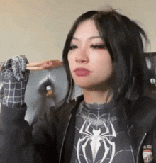 a woman wearing a spider man shirt and gloves is sitting on a chair holding a piece of pizza .