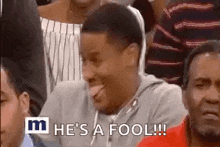 a man is sticking his tongue out while sitting in a crowd of people and making a funny face .