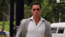 a man wearing sunglasses and a suit is walking down the street .