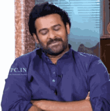 a man in a blue shirt is sitting with his eyes closed and his arms crossed .