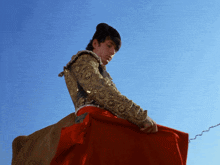 a man in a gold jacket and red skirt is holding a red cloth
