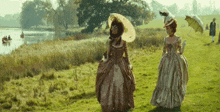 two women in historical costumes are walking in a field .