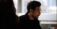 a man with curly hair is sitting in front of a window with a cw logo
