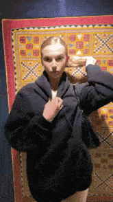 a woman in a black jacket is holding a purse in front of a colorful rug .