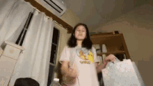 a girl is standing in a room holding a gift bag .