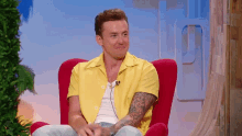 a man in a yellow shirt is sitting in a red chair with a microphone .