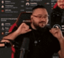 a man with a beard and glasses is sitting in a red and black gaming chair .