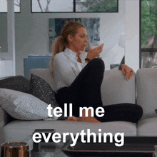 a woman sits on a couch with the words tell me everything written on the bottom