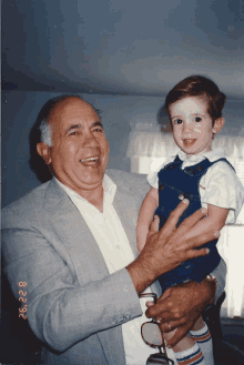 a man in a suit holds a young boy in his arms and the date of the photo is 8.2.2.93