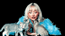 a blonde woman in a blue feathered coat is holding two kittens