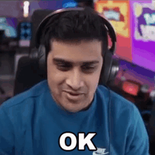 a man wearing headphones and a blue shirt is sitting in front of a computer and saying ok .