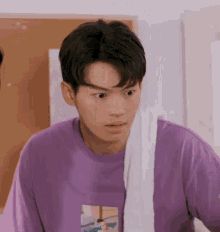 a young man wearing a purple t-shirt and a white towel around his neck .