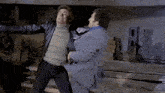 a man in a suit and a man in a turtleneck are fighting each other
